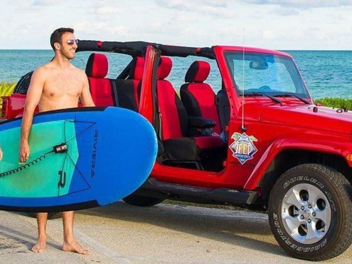 a woman standing in front of a blue car parked on a beach
